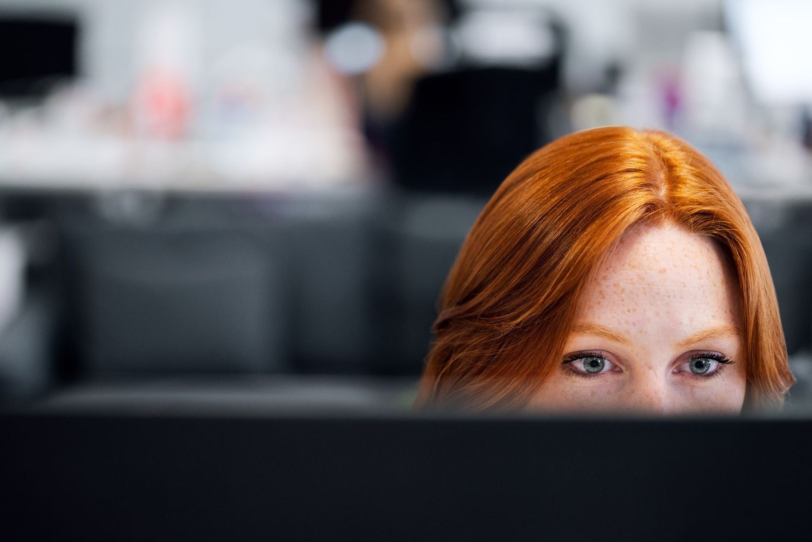Red-haired woman focused behind a large computer monitor
